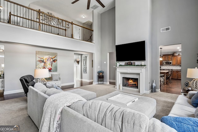 carpeted living area with visible vents, a fireplace with flush hearth, baseboards, and a ceiling fan