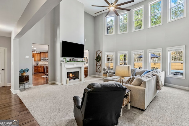 living area featuring wood finished floors, baseboards, a fireplace with flush hearth, and ceiling fan