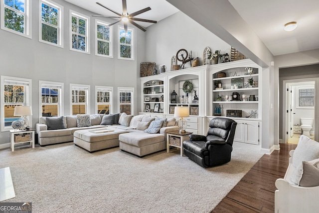 living area with baseboards, a high ceiling, dark wood-style flooring, and a ceiling fan