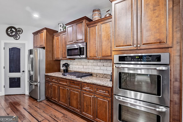 kitchen with tasteful backsplash, appliances with stainless steel finishes, light stone counters, and dark wood-style flooring