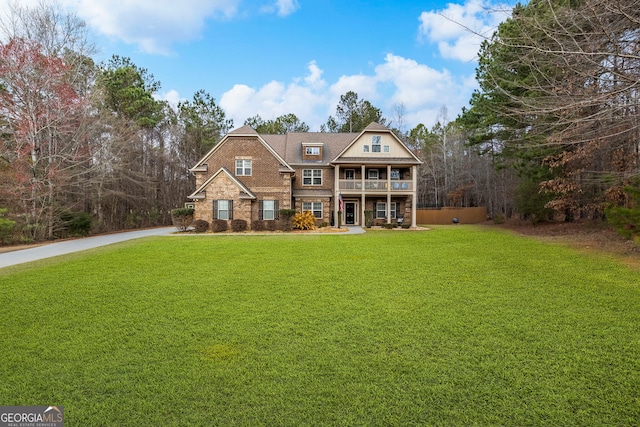 view of front of property with brick siding, driveway, a balcony, and a front lawn