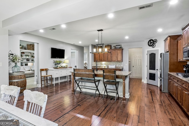 kitchen featuring light stone countertops, a center island with sink, dark wood finished floors, a breakfast bar, and appliances with stainless steel finishes