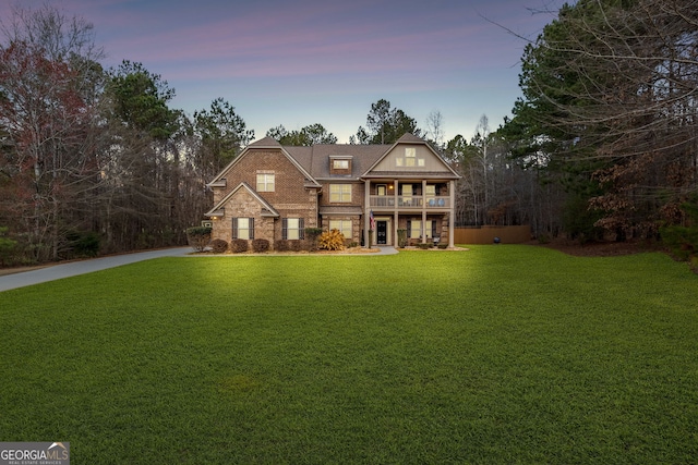 view of front of home featuring a front yard, a balcony, concrete driveway, stone siding, and brick siding