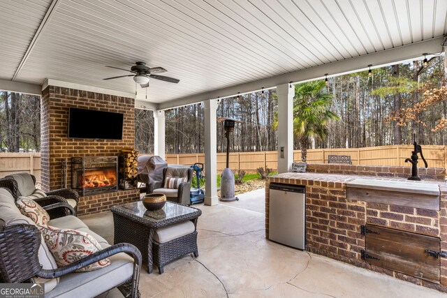 view of patio with a ceiling fan, an outdoor living space with a fireplace, and a fenced backyard