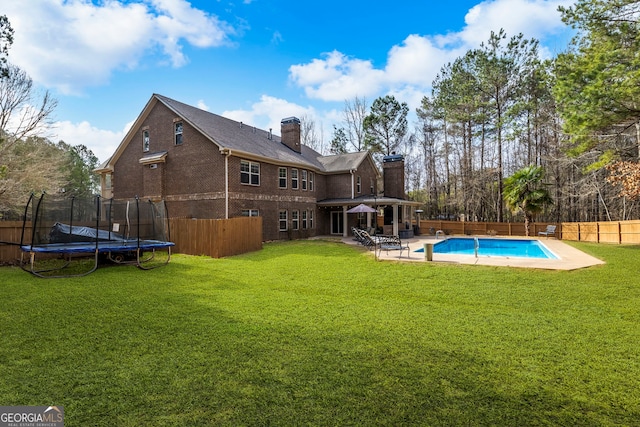 back of house featuring a fenced in pool, a trampoline, a chimney, a fenced backyard, and a yard