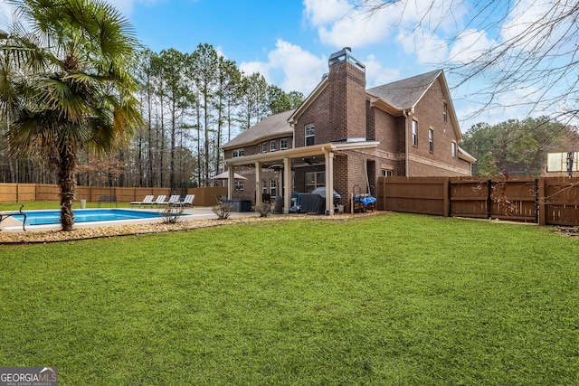 rear view of property featuring a lawn, brick siding, a fenced backyard, and a chimney