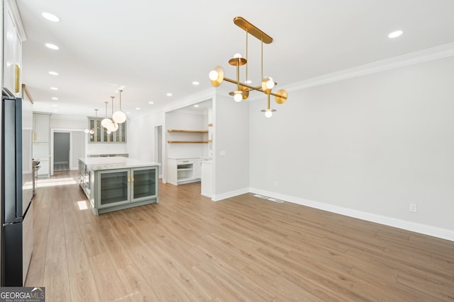 kitchen with light wood-style flooring, freestanding refrigerator, ornamental molding, light countertops, and a notable chandelier