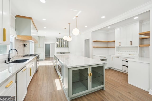 kitchen featuring stainless steel gas range oven, light wood-type flooring, custom range hood, open shelves, and a sink