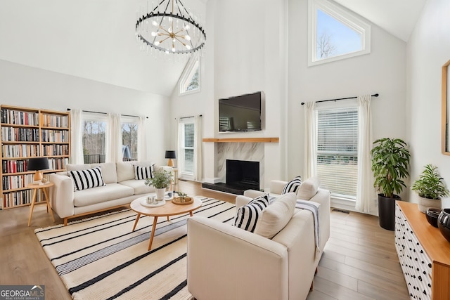 living area featuring visible vents, light wood finished floors, high vaulted ceiling, an inviting chandelier, and a high end fireplace