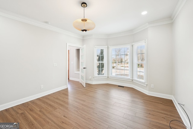 empty room with visible vents, crown molding, baseboards, and wood finished floors