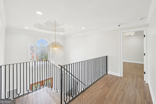 hall featuring baseboards, a tray ceiling, ornamental molding, an upstairs landing, and wood finished floors