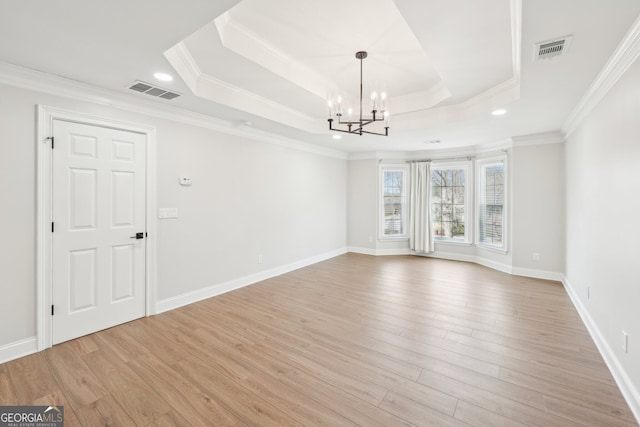 spare room with a tray ceiling, visible vents, light wood-type flooring, and a notable chandelier