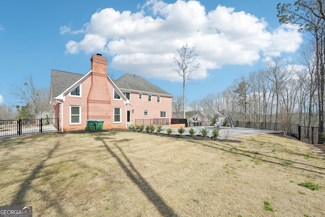 rear view of house featuring brick siding, a chimney, a yard, and fence