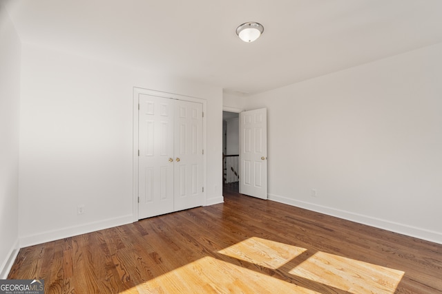 unfurnished bedroom featuring wood finished floors, baseboards, and a closet