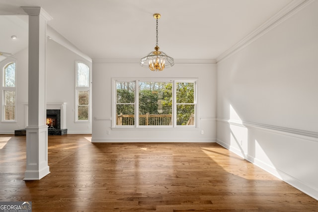 unfurnished dining area featuring wood finished floors, baseboards, a fireplace, crown molding, and a chandelier