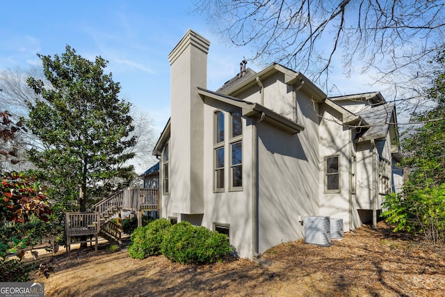 view of property exterior featuring stucco siding, a chimney, and stairs