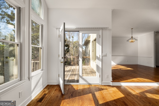 doorway with a notable chandelier, wood finished floors, visible vents, and baseboards