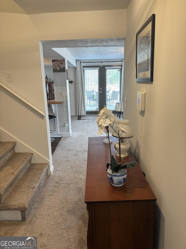 hallway with french doors, carpet, stairs, and a textured ceiling