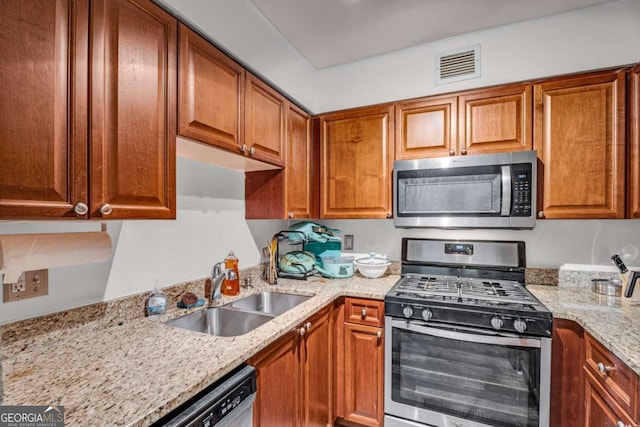 kitchen featuring light stone countertops, visible vents, a sink, stainless steel appliances, and brown cabinets