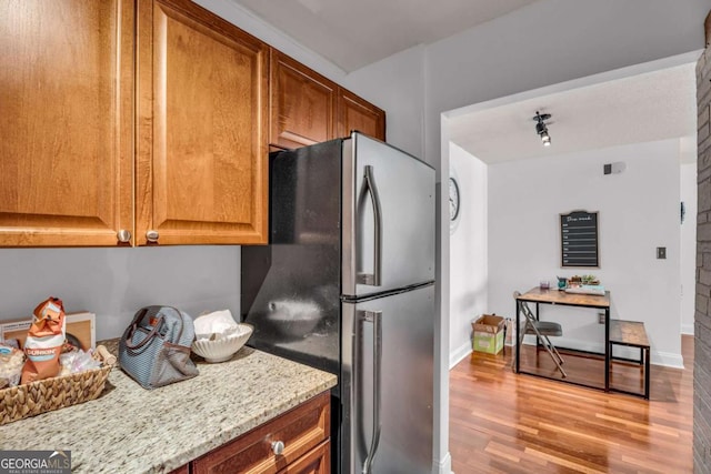 kitchen with light stone countertops, wood finished floors, brown cabinets, and freestanding refrigerator