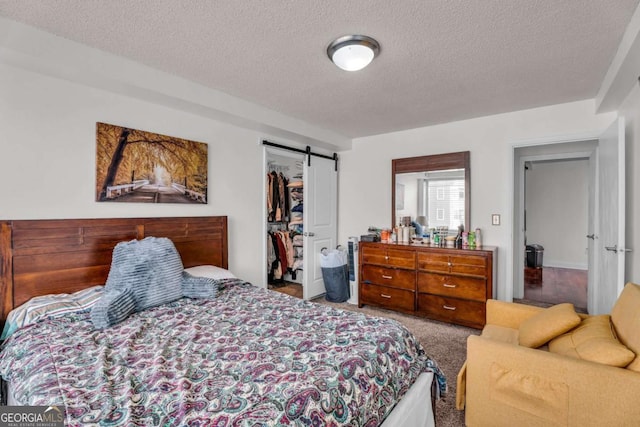 bedroom with carpet floors, a spacious closet, a closet, a textured ceiling, and a barn door