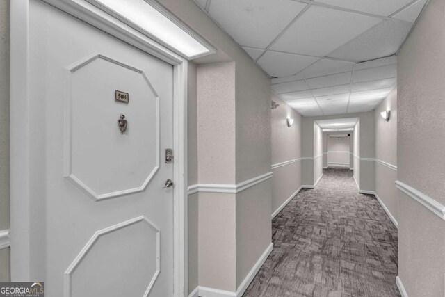 corridor featuring baseboards, a paneled ceiling, and carpet floors