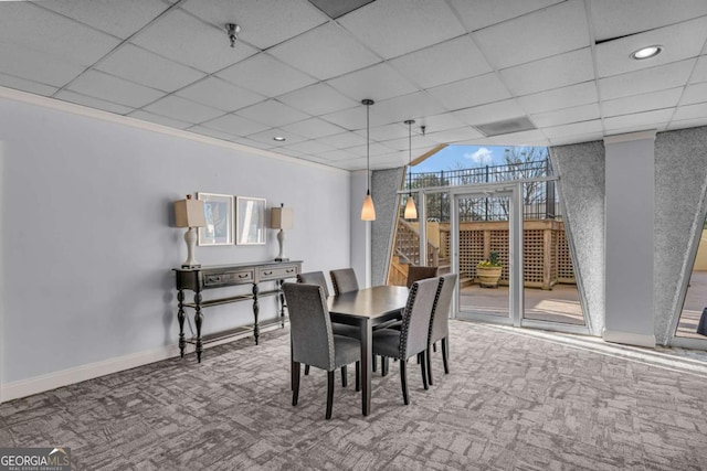 carpeted dining room featuring a drop ceiling, baseboards, and ornamental molding