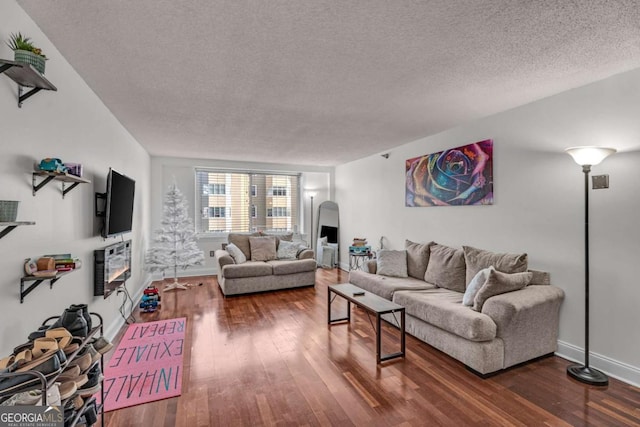 living area featuring baseboards, a textured ceiling, a glass covered fireplace, and dark wood-style flooring