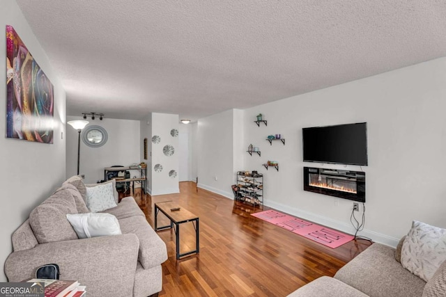 living area with a glass covered fireplace, wood finished floors, baseboards, and a textured ceiling