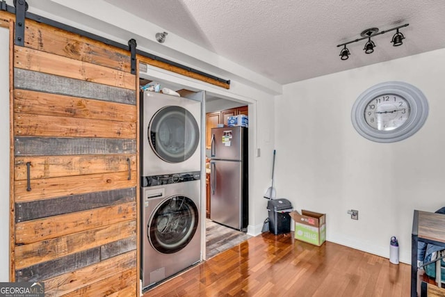 clothes washing area featuring wood finished floors, laundry area, stacked washer and dryer, a textured ceiling, and a barn door