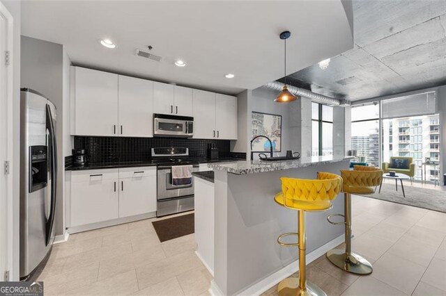 250 Pharr Rd Unit 1702, Atlanta, GA 30305 - kitchen with appliances with stainless steel finishes, tasteful backsplash, white cabinets, decorative light fixtures, and a kitchen bar