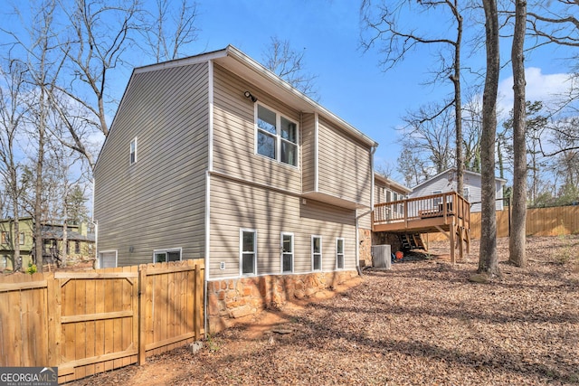 view of property exterior featuring central AC, fence, stone siding, a gate, and a deck