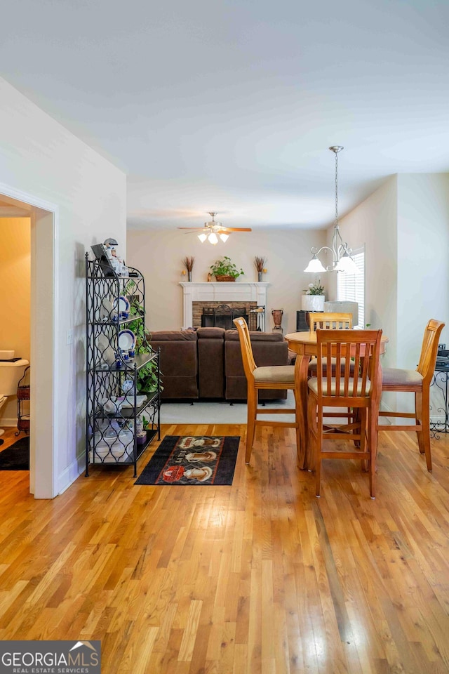 dining area with light wood-type flooring, a ceiling fan, and a fireplace