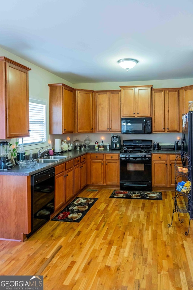 kitchen featuring a sink, brown cabinets, light wood-style floors, and black appliances