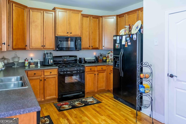 kitchen featuring dark countertops, light wood-type flooring, brown cabinetry, black appliances, and a sink