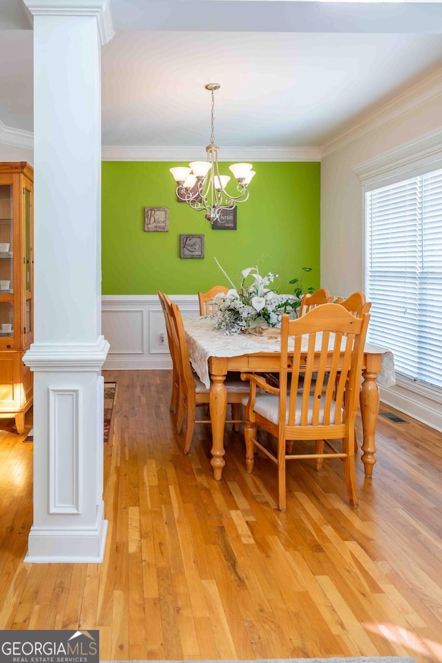 dining area featuring visible vents, crown molding, a wainscoted wall, light wood-type flooring, and a notable chandelier