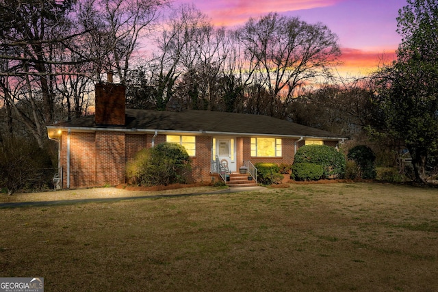 view of front of home featuring brick siding, a chimney, and a yard