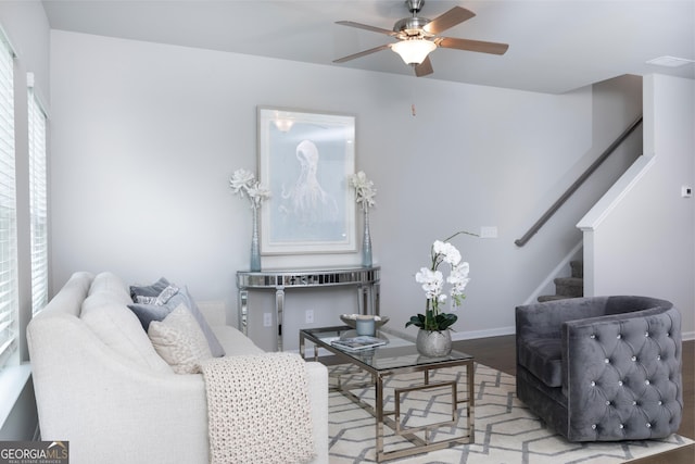 living area featuring wood finished floors, baseboards, ceiling fan, and stairs