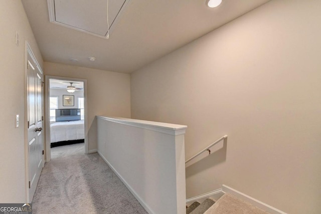 hallway with carpet, attic access, an upstairs landing, and baseboards