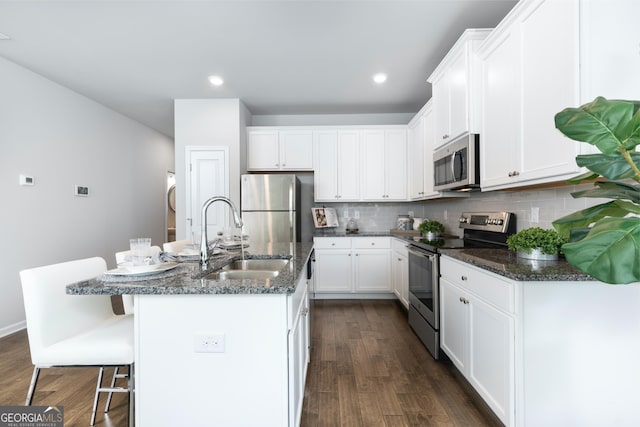 kitchen with dark wood-style flooring, a sink, stainless steel appliances, white cabinetry, and backsplash