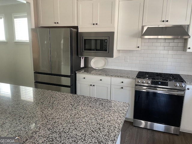 kitchen with under cabinet range hood, backsplash, light stone countertops, and appliances with stainless steel finishes