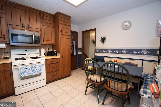 1972 Cox Dr, Austell, GA 30168 - kitchen featuring light countertops, white range with gas cooktop, stainless steel microwave, and a wainscoted wall