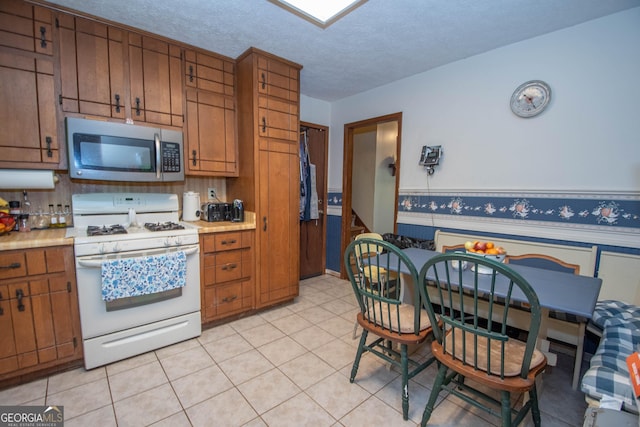 1972 Cox Dr, Austell, GA 30168 - kitchen with white range with gas stovetop, light countertops, stainless steel microwave, a wainscoted wall, and brown cabinets
