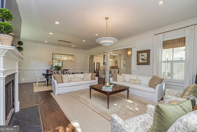 living area with dark wood finished floors, a fireplace with flush hearth, wainscoting, crown molding, and a decorative wall