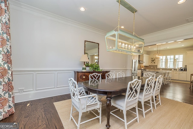 dining area featuring a notable chandelier, wainscoting, crown molding, and wood finished floors