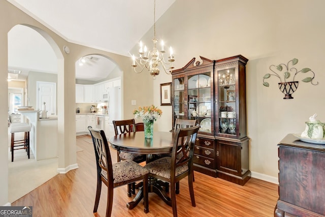 dining area with baseboards, lofted ceiling, arched walkways, and light wood finished floors