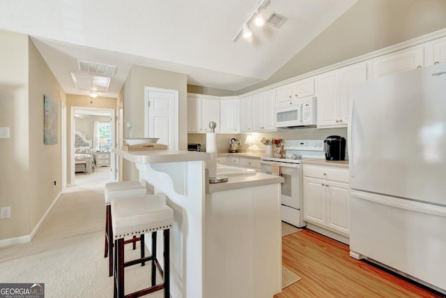 kitchen featuring visible vents, white appliances, a breakfast bar area, and lofted ceiling