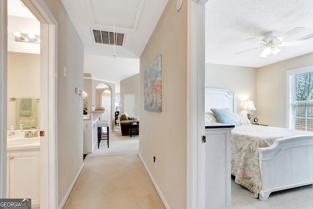 hall featuring visible vents, a sink, baseboards, light colored carpet, and attic access