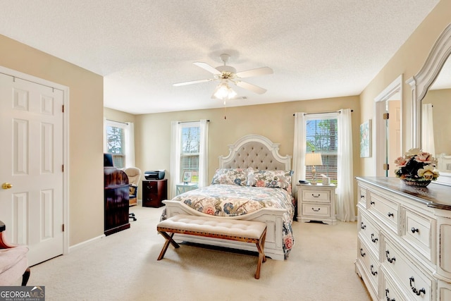 bedroom with multiple windows, light carpet, a textured ceiling, and a ceiling fan