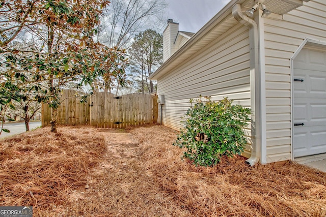 view of side of property with a chimney, a garage, and fence